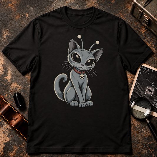 A black short-sleeve crewneck t-shirt featuring a cartoon graphic of a gray cat with large eyes, antennae, and a red collar, displayed against a textured gray background.