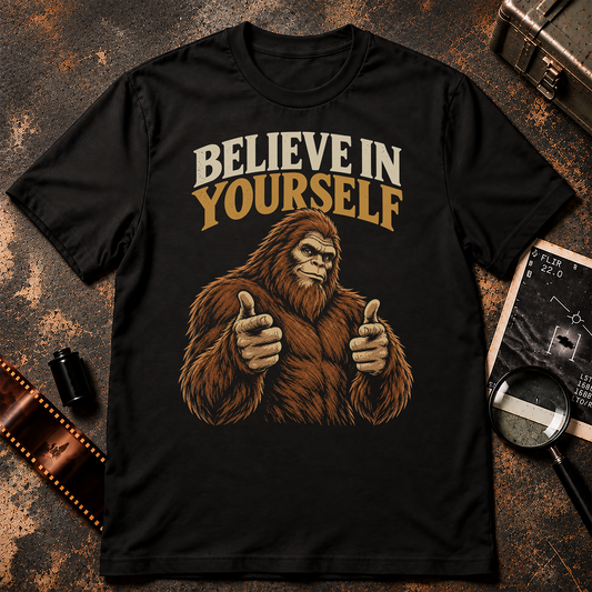 Brown Bigfoot giving finger guns beneath retro cream and gold text reading Believe in Yourself on a black background.