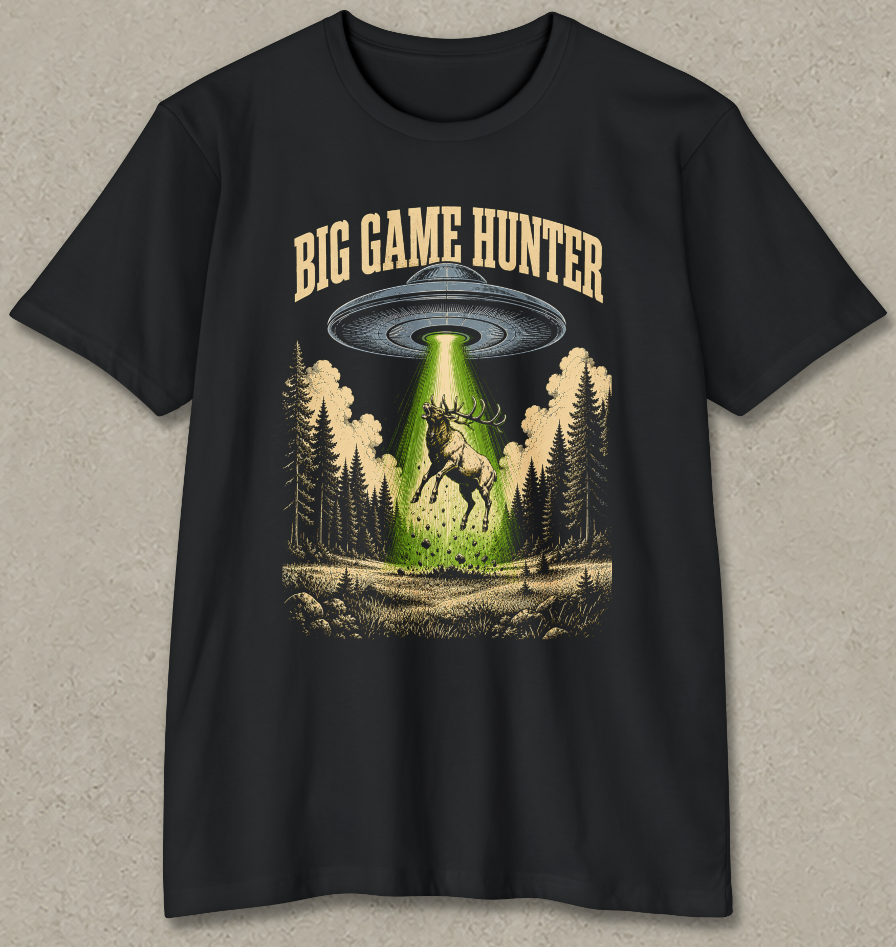 A black short-sleeve graphic t-shirt featuring a 'Big Game Hunter' theme. The graphic shows a green beam from a UFO shining down onto a deer in a forest, with the text 'BIG GAME HUNTER' printed above in a tan serif font.