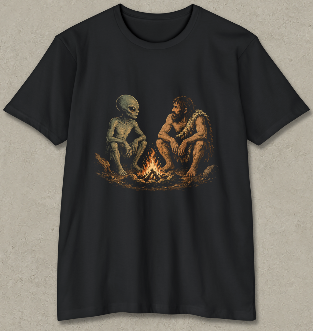 A black short-sleeve crewneck t-shirt featuring a graphic print of a prehistoric man and an alien sitting together around a campfire, displayed against a textured gray background.