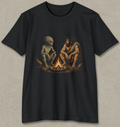 A black short-sleeve crewneck t-shirt featuring a graphic print of a prehistoric man and an alien sitting together around a campfire, displayed against a textured gray background.