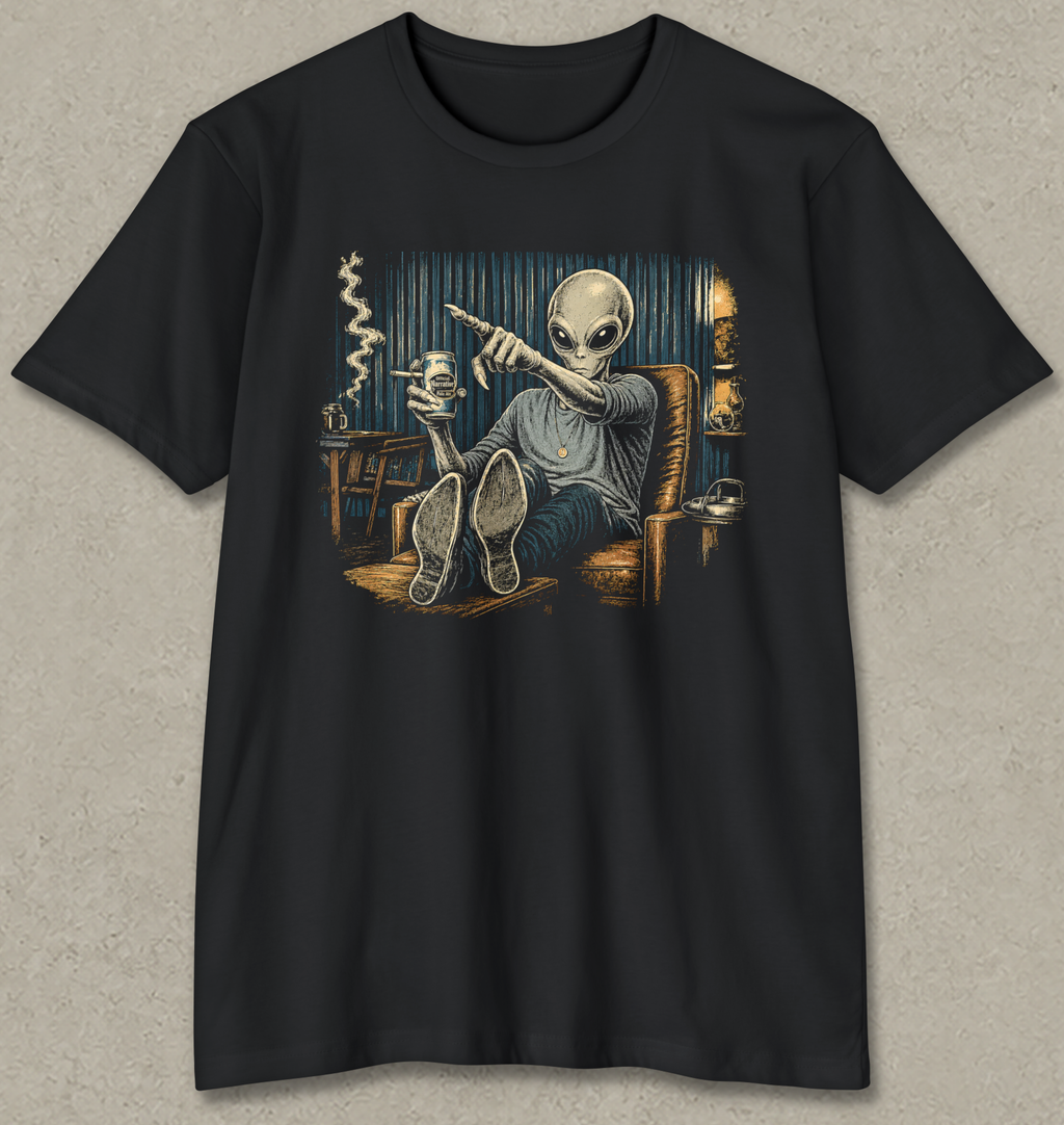 A black short-sleeve crewneck t-shirt featuring a detailed graphic print of a grey alien sitting in a leather chair and pointing a gun, displayed against a textured light gray background.
