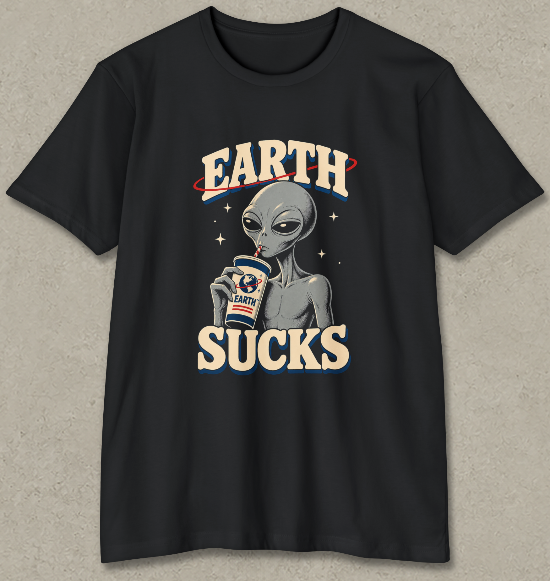 A black short-sleeve graphic t-shirt featuring a retro-style alien holding a coffee cup with 'EARTH' written above and 'SUCKS' below, displayed on a textured gray background.