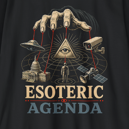 A close-up of a black graphic t-shirt featuring a detailed esoteric design. The graphic shows a hand with manicured nails pulling marionette strings over an eye-in-a-pyramid, with icons of a UFO, surveillance camera, globe, capitol building, and satellite.