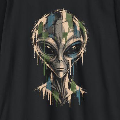 A close-up of a black t-shirt featuring a stylized alien graphic with a dripping paint effect in green, blue, beige, and gray.