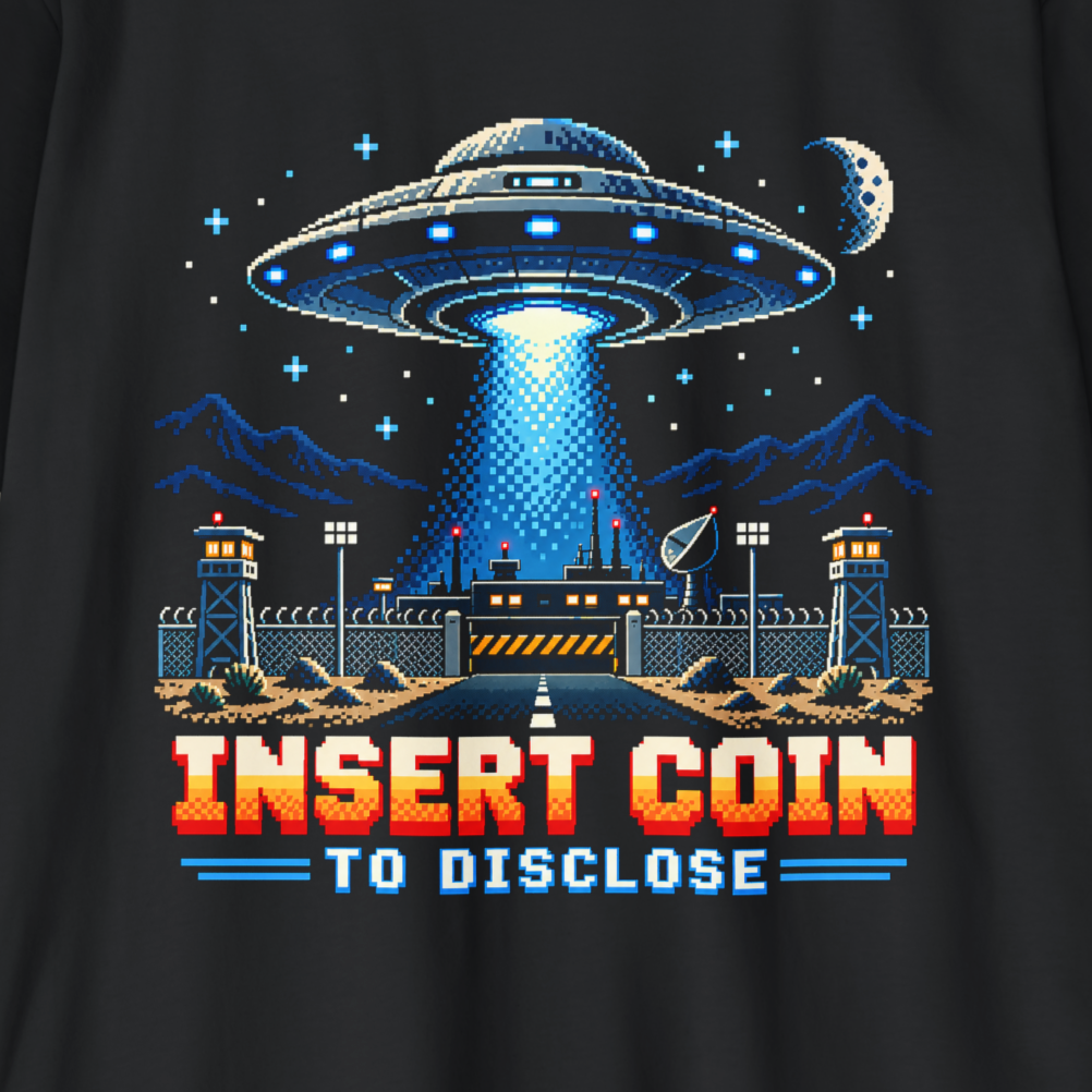 A close-up of a black t-shirt featuring a retro 8-bit pixel art graphic of a UFO landing site with a beam of light, mountains, a moon, and the text 'INSERT COIN TO DISCLOSE' in red and blue.