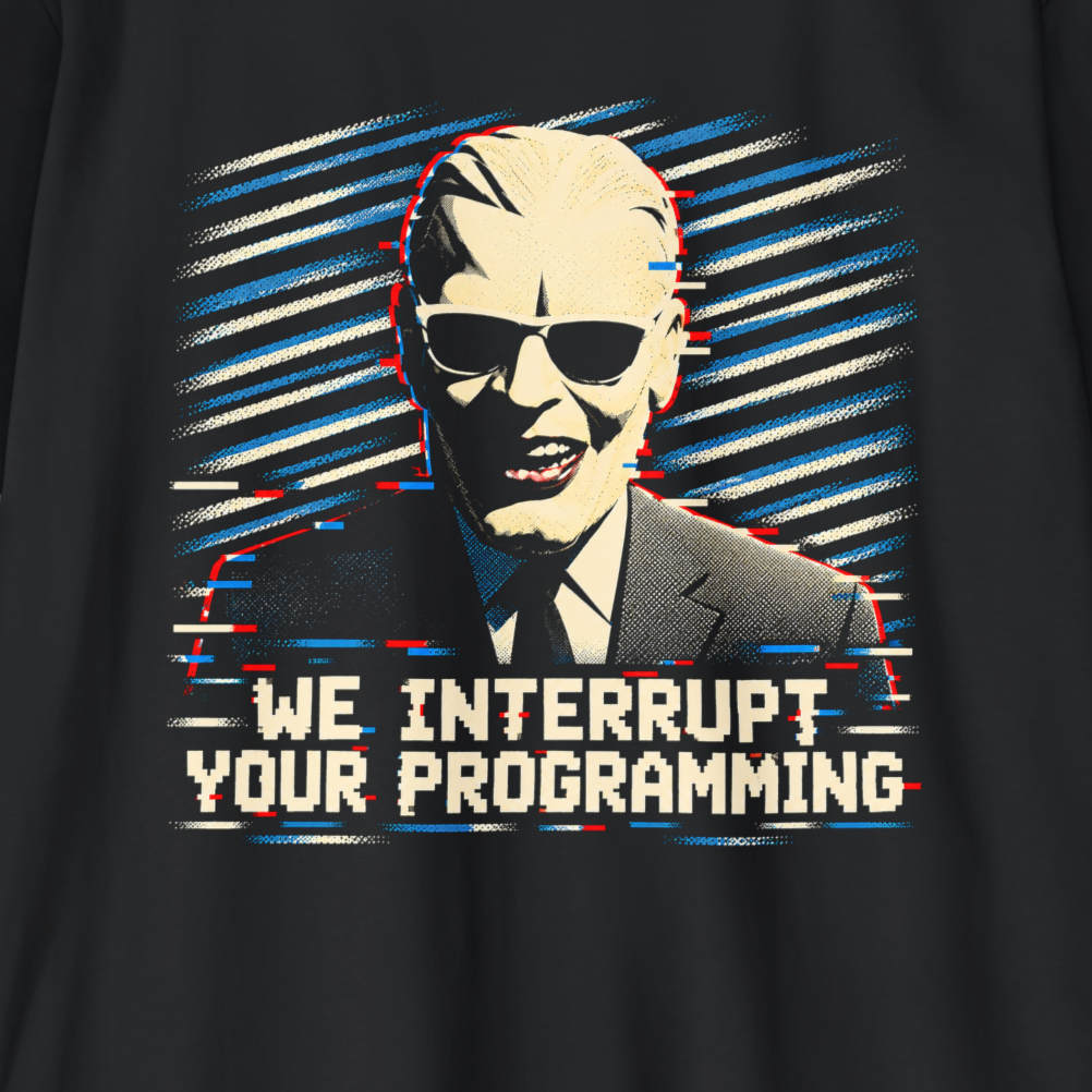 A close-up of a black t-shirt featuring a graphic print of Karl Lagerfeld wearing sunglasses and a suit, with the text 'WE INTERRUPT YOUR PROGRAMMING' in a retro computer-style font.