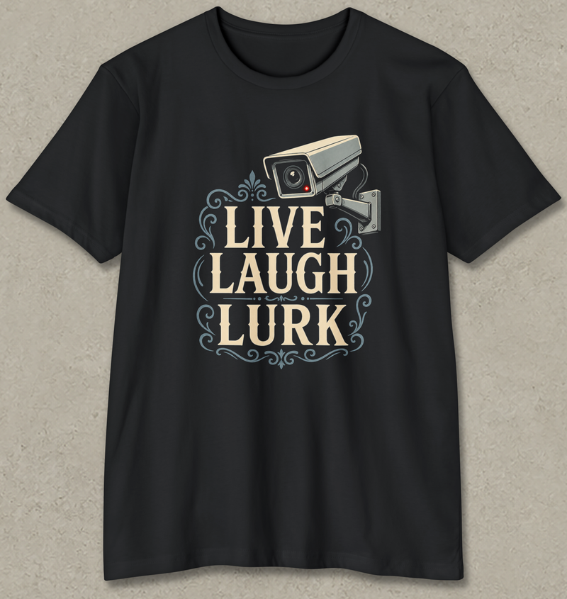 A black short-sleeve crewneck t-shirt with a graphic on the front featuring a security camera and the text 'LIVE LAUGH LURK' in beige and light blue, displayed against a textured gray background.