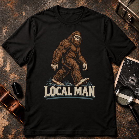 Bigfoot walking through the woods above large cream LOCAL MAN text in a retro comic-style graphic.