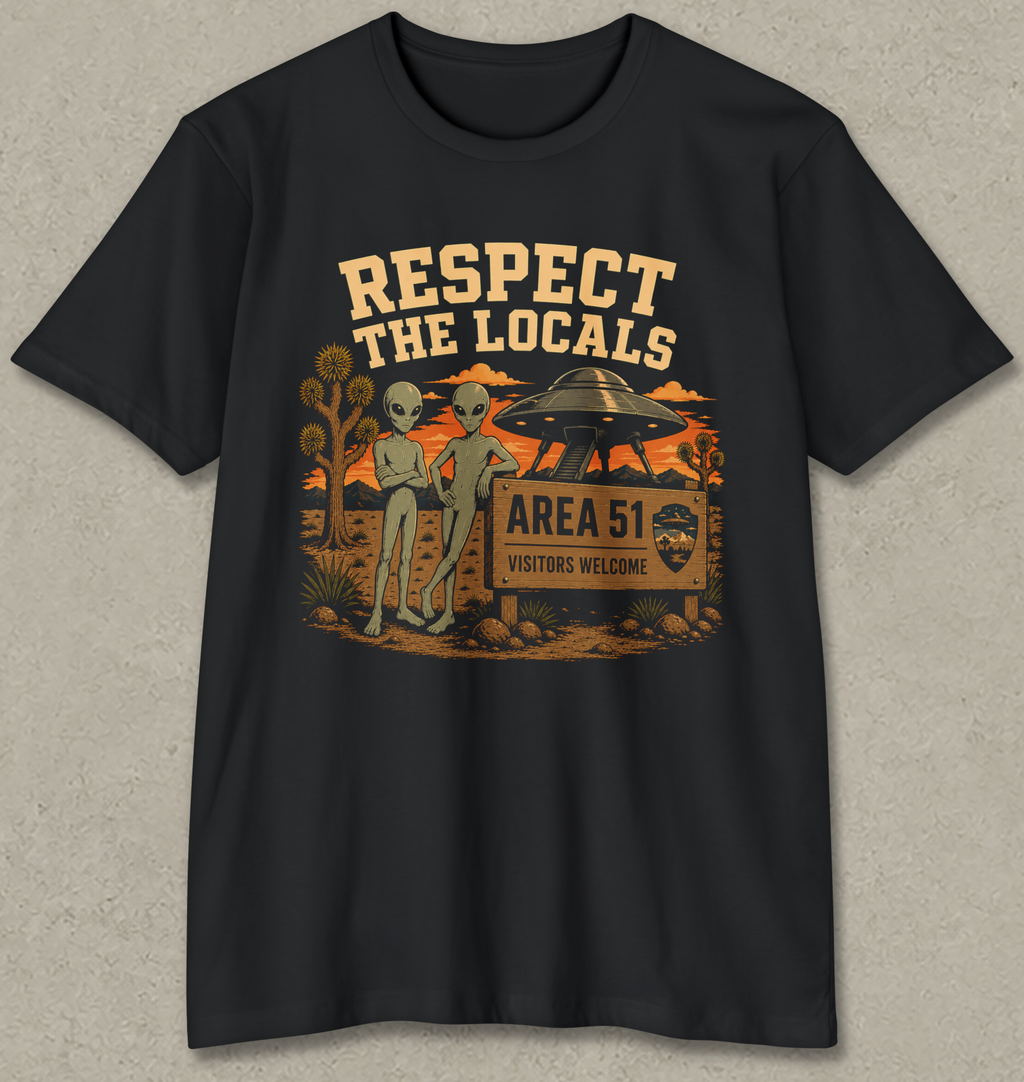 A black short-sleeve crewneck t-shirt with a retro-style graphic on the front. The graphic features two green aliens standing next to a wooden sign that reads 'AREA 51 VISITORS WELCOME' under a sign reading 'RESPECT THE LOCALS'.