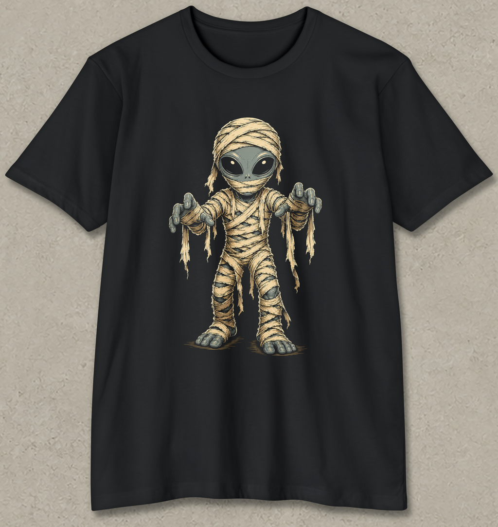 A black short-sleeve crewneck t-shirt featuring a cartoon graphic of a mummy alien with large eyes and outstretched hands, displayed flat against a textured gray background.