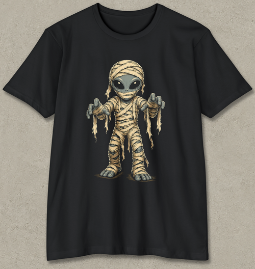 A black short-sleeve crewneck t-shirt featuring a cartoon graphic of a mummy alien with large eyes and outstretched hands, displayed flat against a textured gray background.