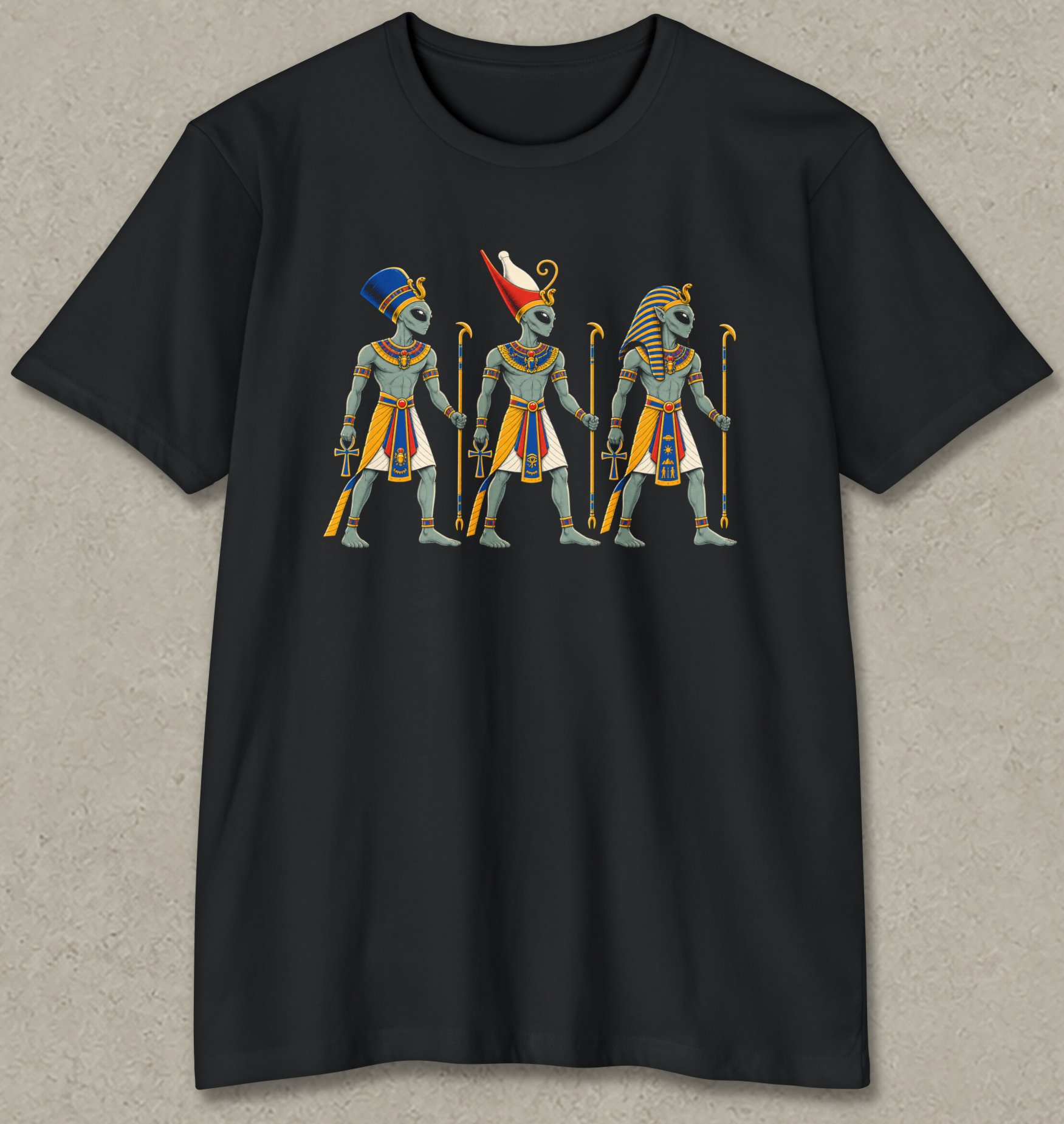 A black short-sleeve crewneck t-shirt with a graphic print of three ancient Egyptian figures in headdresses and robes, displayed flat against a textured gray background.