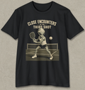 A black short-sleeve crewneck t-shirt with a vintage-style graphic of an alien playing pickleball on a court, with the text 'CLOSE ENCOUNTERS OF THE THIRD SHOT' printed above it. The t-shirt is displayed flat against a textured gray background.