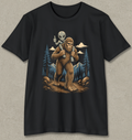 A black short-sleeve crewneck t-shirt featuring a graphic print of a brown furry Bigfoot carrying a small gray alien on his shoulders, set against a pine forest background.