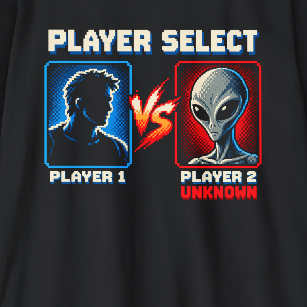Close-up of a black graphic print on a shirt featuring retro pixel-art text reading 'PLAYER SELECT' with a blue silhouette labeled 'PLAYER 1' and a gray alien labeled 'PLAYER 2 UNKNOWN' separated by a red-orange 'VS'.