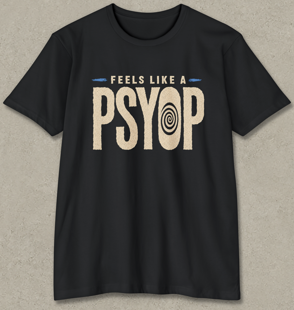A black short-sleeve crewneck t-shirt with a distressed graphic on the chest that reads 'FEELS LIKE A PSYOP' in beige, with a spiral eye motif inside the letter 'O'. The t-shirt is displayed flat against a textured gray background.