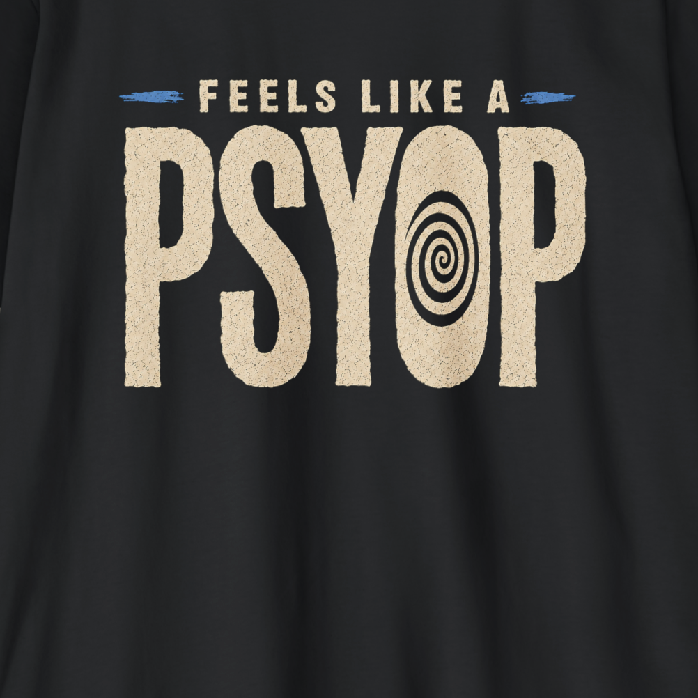 A close-up of a black t-shirt featuring a distressed beige graphic that reads 'FEELS LIKE A PSYOP' with a spiral eye design inside the letter O.