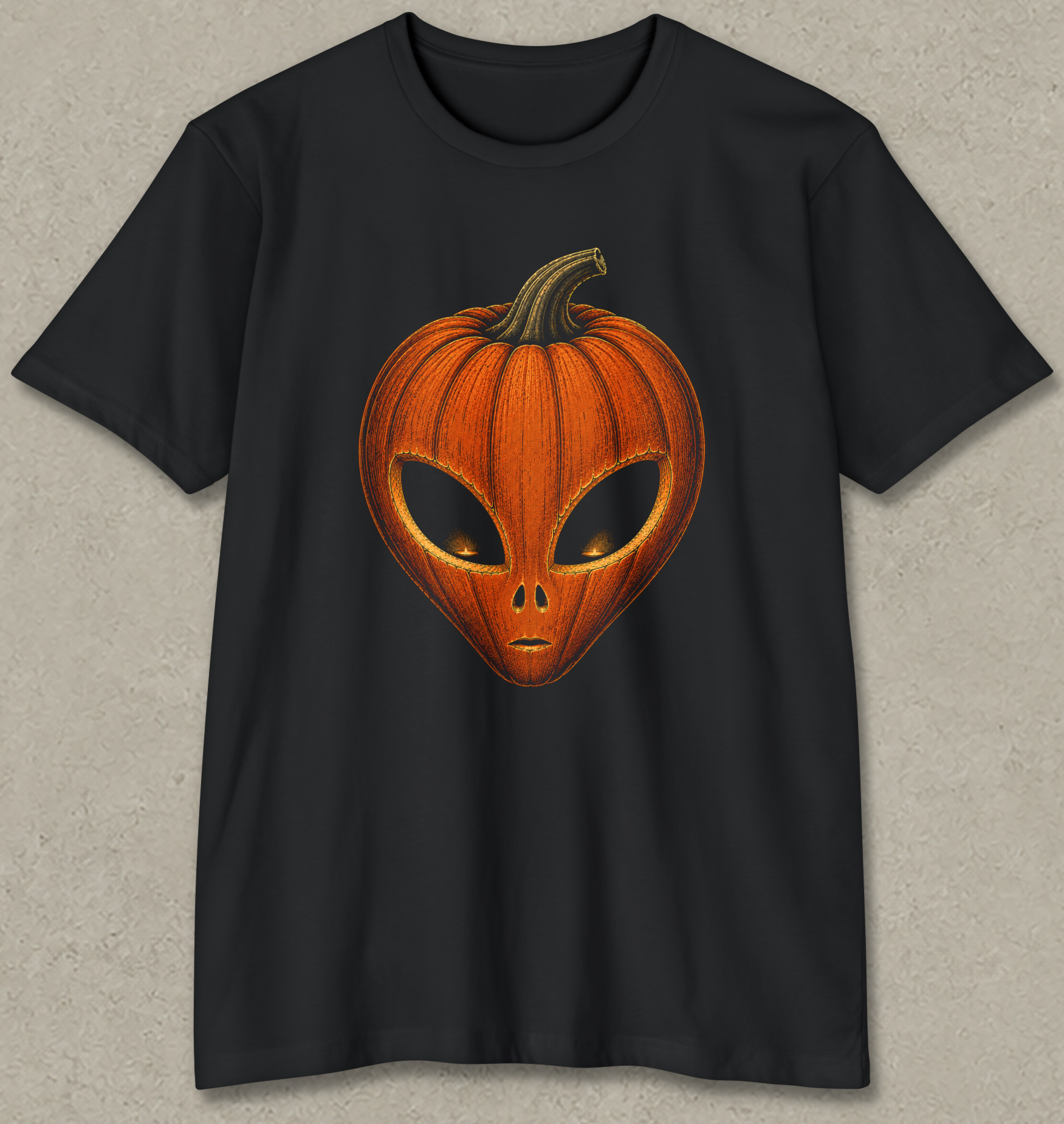 A black short-sleeve crewneck t-shirt featuring a graphic of a carved orange pumpkin shaped like an alien head, displayed against a textured gray background.