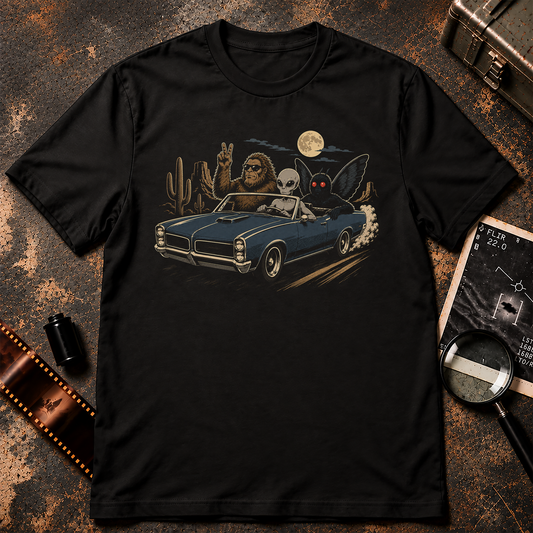 Cryptid Road Trip shirt design featuring Bigfoot, a grey alien, and Mothman riding in a blue convertible through the desert under a full moon.
