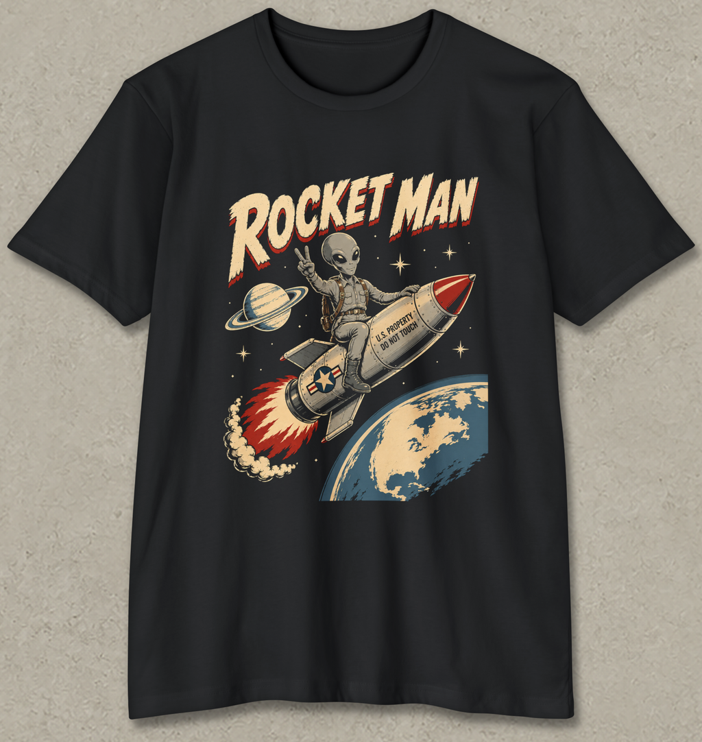 A black short-sleeve crewneck t-shirt featuring a retro-style graphic of an alien riding a rocket ship with the text 'ROCKET MAN' above it, set against a textured gray background.