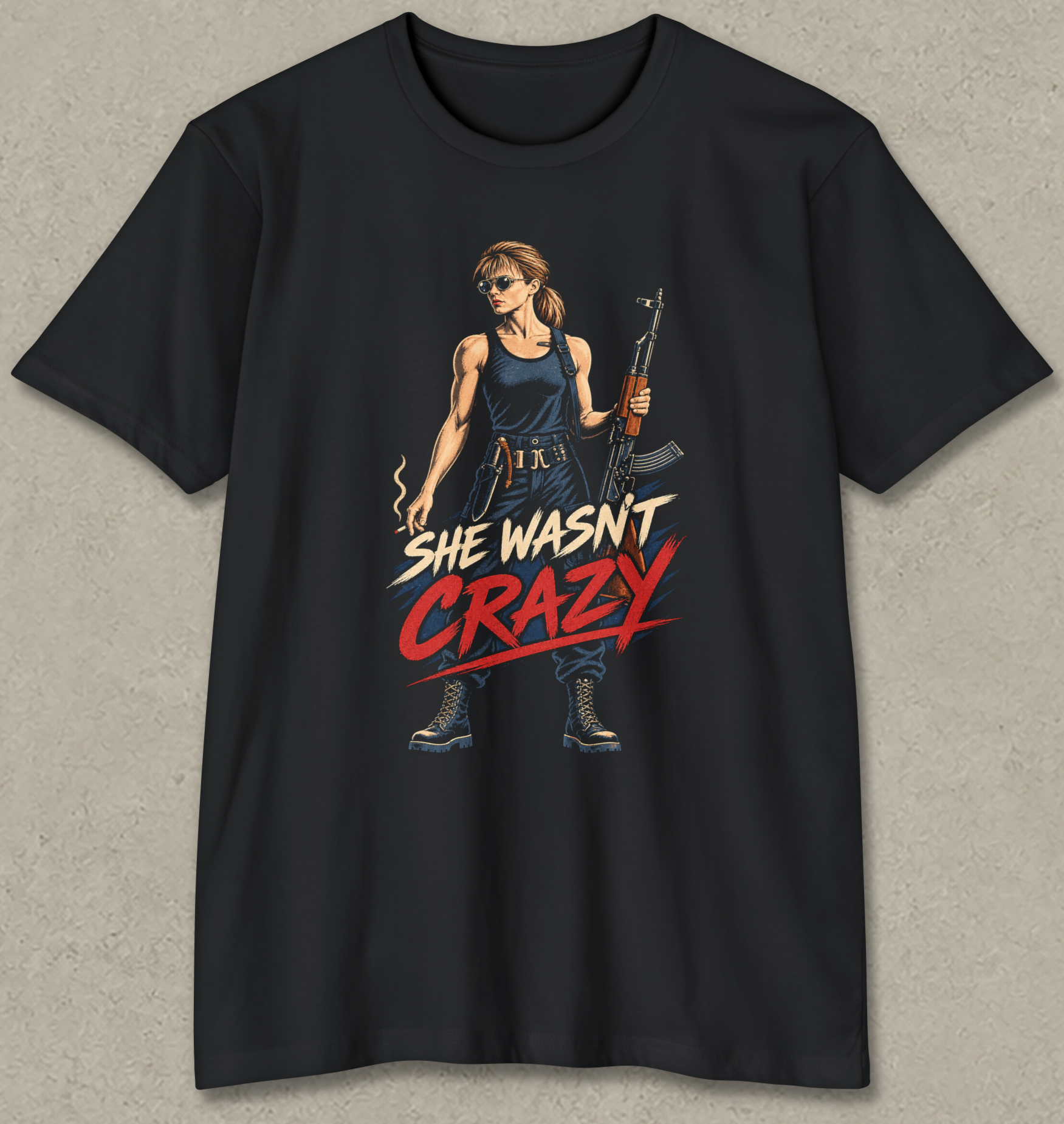 A black short-sleeve crewneck t-shirt with a graphic print of a woman holding an assault rifle, with the text 'SHE WASN'T CRAZY' in stylized red and white lettering.
