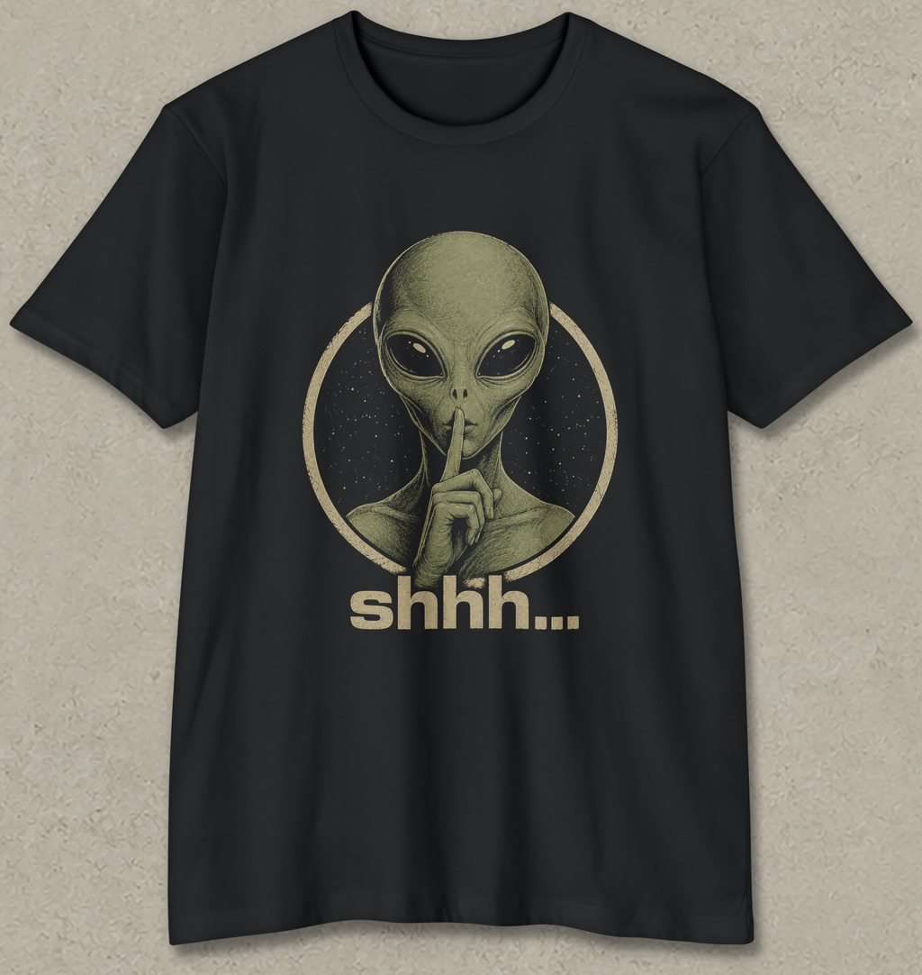 A black short-sleeve crewneck t-shirt featuring a vintage-style graphic of an alien with its finger to its lips inside a circle, with the word 'shhh.