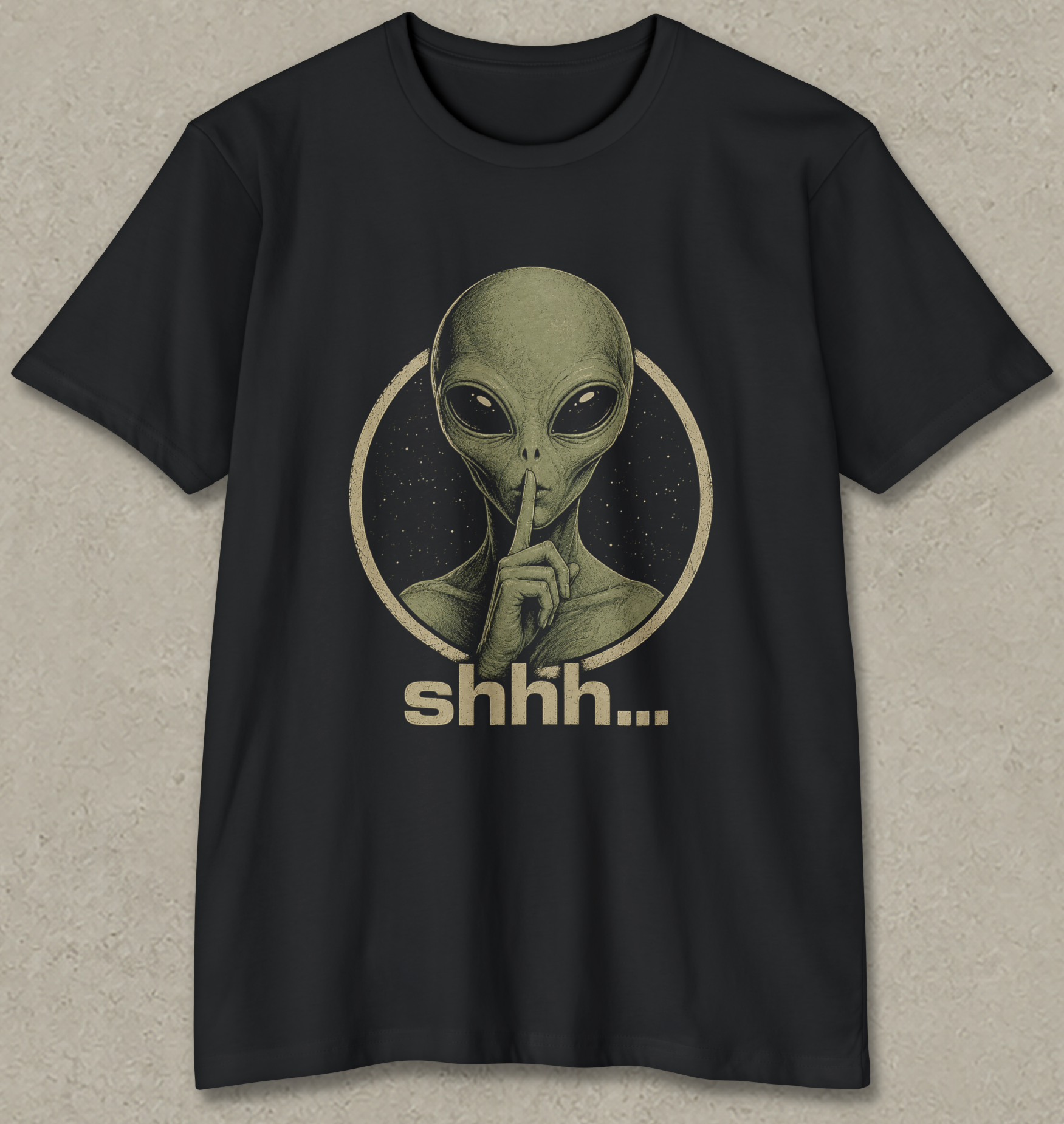 A black short-sleeve crewneck t-shirt featuring a vintage-style graphic of an alien with its finger to its lips inside a circle, with the word 'shhh.
