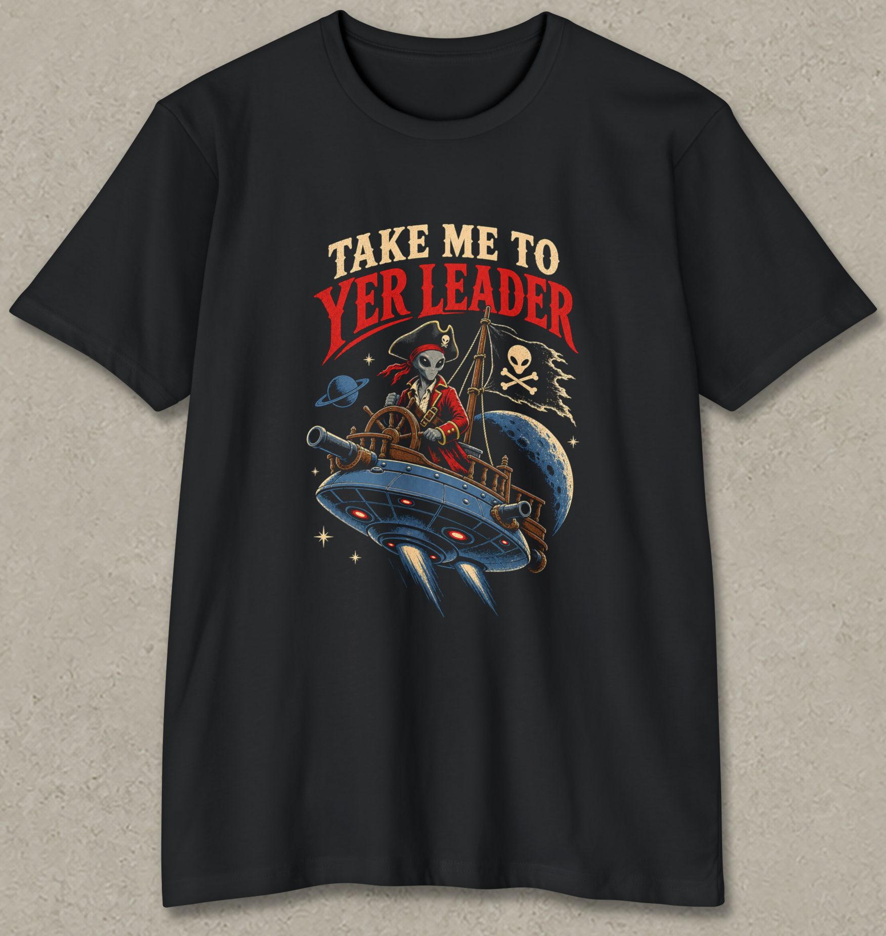 A black short-sleeve crewneck t-shirt featuring a pirate-themed graphic on the front. The graphic shows a skeleton pirate in a red hat and coat flying a blue spaceship under a red and beige text bubble that reads 'TAKE ME TO YER LEADER'.