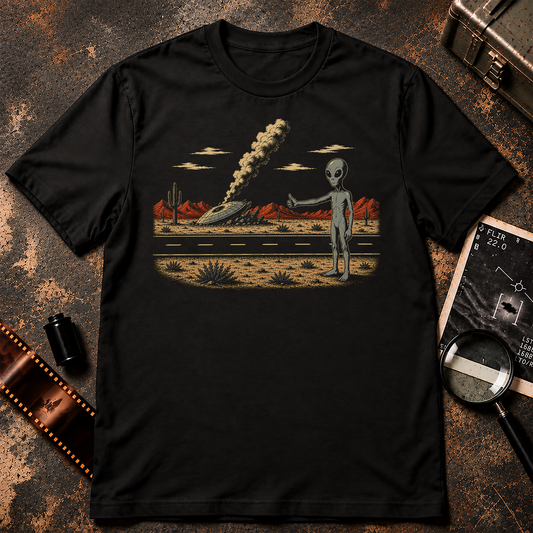 STRANDED retro sci-fi design featuring a grey alien hitchhiking beside a desert highway with a crashed, smoking flying saucer in the background.