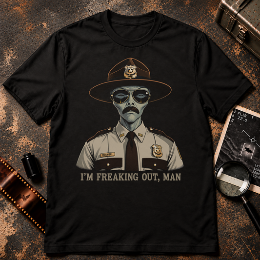 Grey alien state trooper wearing a campaign hat, aviator sunglasses, mustache and Roswell nameplate above the words I’m Freaking Out, Man.
