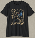 A black short-sleeve crewneck t-shirt with a graphic print of a creature resembling a bat or owl with glowing red eyes, reaching toward a hanging blue light. The text 'DRAWN TO THE LIGHT' is printed below in a stylized beige font.