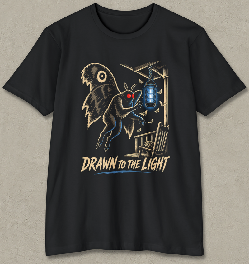 A black short-sleeve crewneck t-shirt with a graphic print of a creature resembling a bat or owl with glowing red eyes, reaching toward a hanging blue light. The text 'DRAWN TO THE LIGHT' is printed below in a stylized beige font.