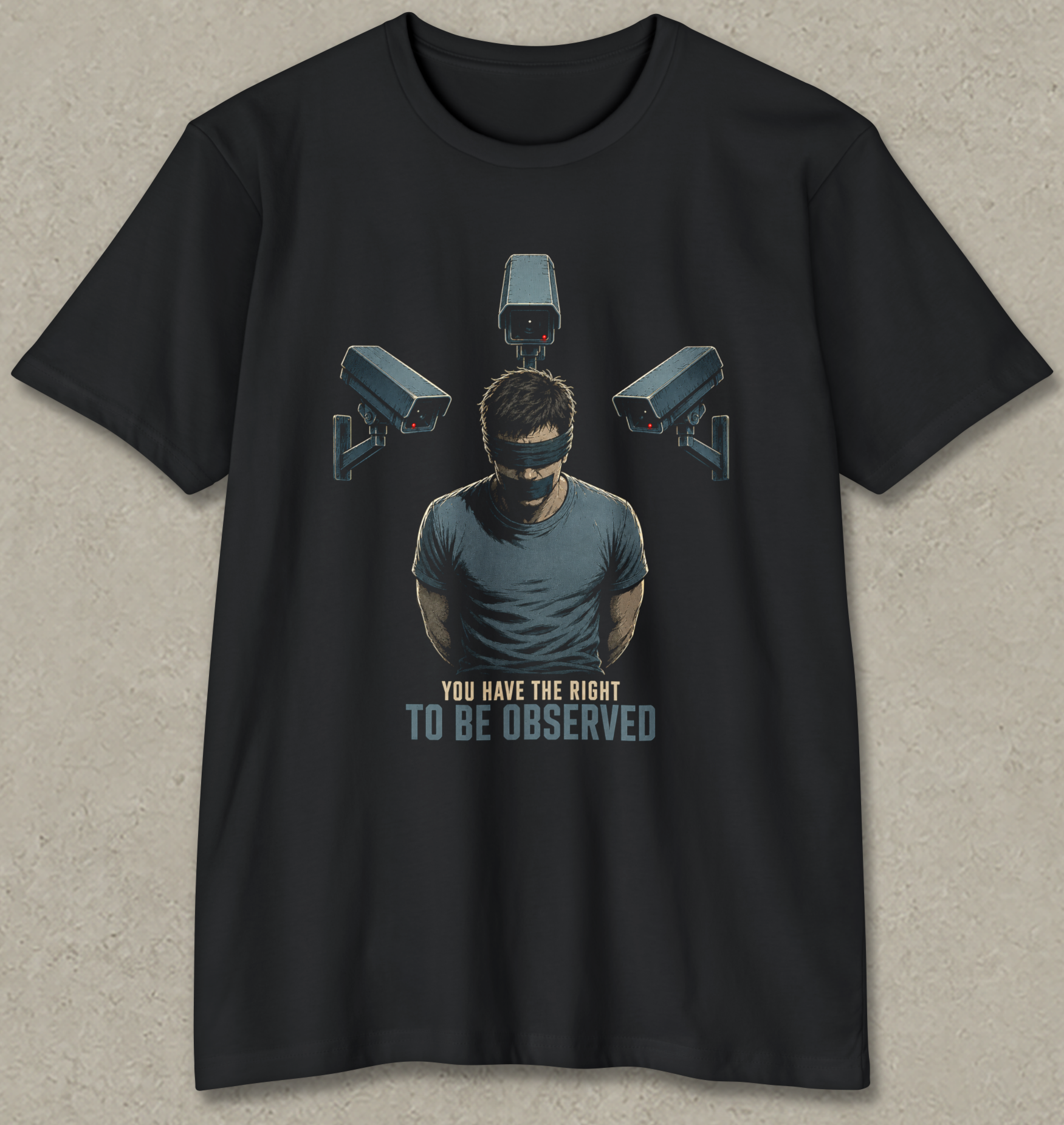 A black short-sleeve t-shirt with a graphic print of a man wearing a blindfold and eyepatch, surrounded by three security cameras, with the text 'YOU HAVE THE RIGHT TO BE OBSERVED' underneath, displayed on a textured gray background.