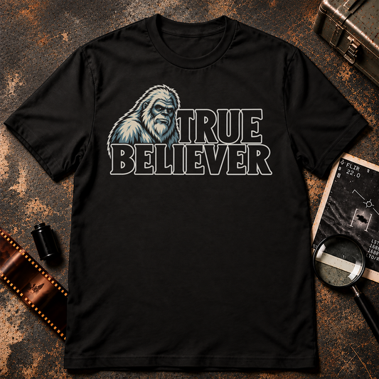 TRUE BELIEVER shirt design featuring a cream and icy blue-grey Yeti portrait beside bold black lettering with cream outlines on a black background.