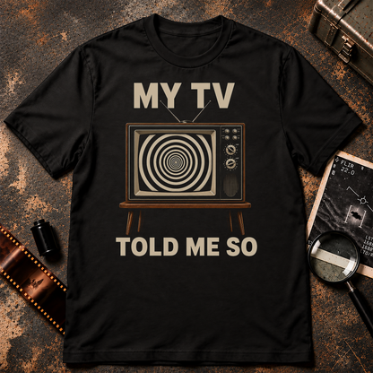 Satirical retro graphic featuring a vintage wood-trim television with antennas and control dials displaying a black-and-cream hypnotic spiral. Large cream text above and below the television reads “MY TV TOLD ME SO” against a black background.