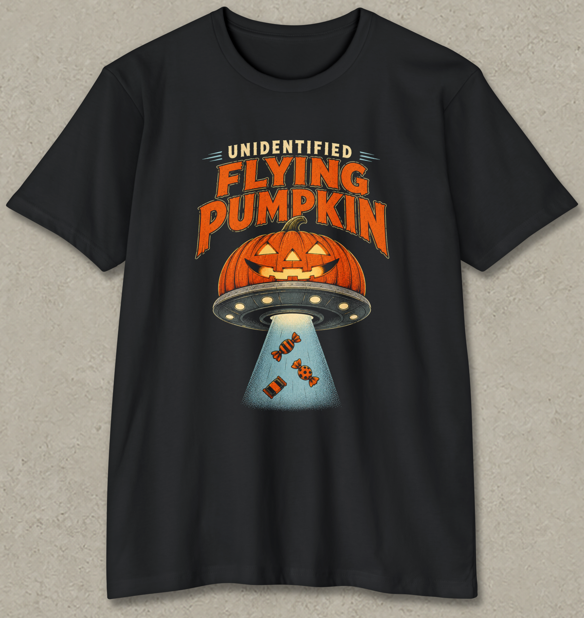 A black short-sleeve crewneck t-shirt with a graphic print of a jack-o'-lantern pumpkin inside a flying UFO emitting a beam of light with candy, and the text 'UNIDENTIFIED FLYING PUMPKIN' in orange and white.