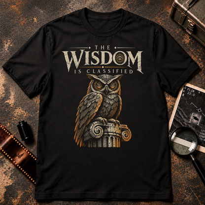 The Wisdom Is Classified T-Shirt design featuring a detailed owl with orange all-seeing eye symbols perched on an ancient stone column. Distressed cream typography reads THE WISDOM IS CLASSIFIED, with orange accents and a black background.